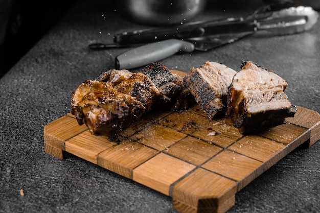 Costillas a la parrilla en rodajas sobre una placa de madera sobre una superficie gris. Decoración de barbacoa.