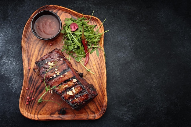 Costillas a la parrilla con salsa y hierbas sobre una tabla de madera