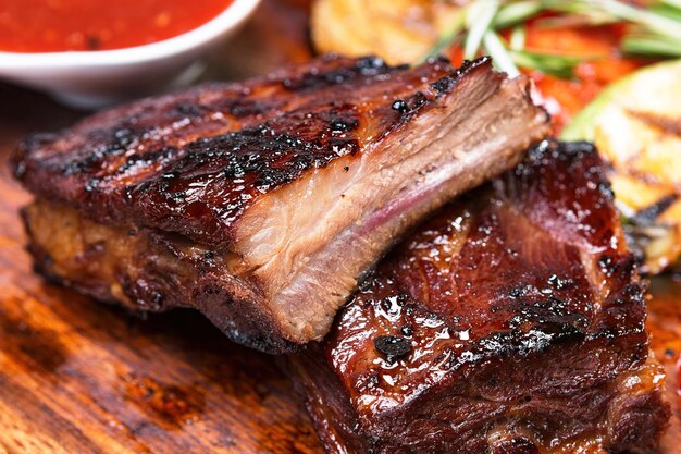 Costillas a la parrilla con salsa en una tabla de madera con verduras