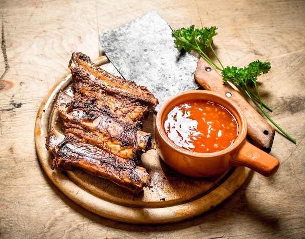 Costillas a la parrilla con salsa de tomate y un hacha de talla sobre fondo de madera