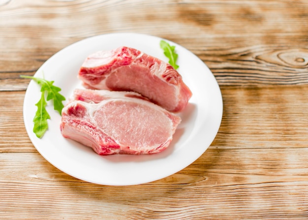 Costillas de pechuga de cerdo cruda en un plato blanco sobre un fondo de madera