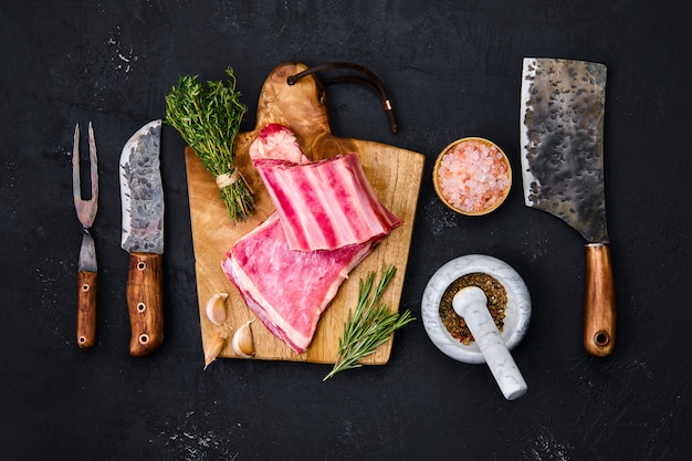 Costillas de pechuga de cordero cruda fresca sobre tabla de cortar de madera con hierbas y condimentos