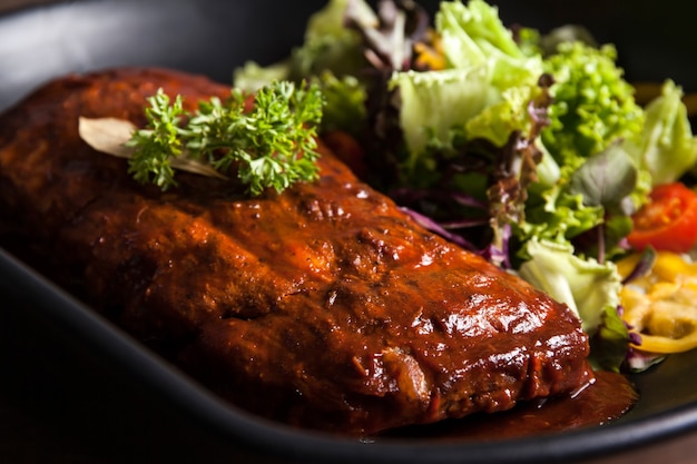 Costillas con salsa y ensalada fresca en una placa negra