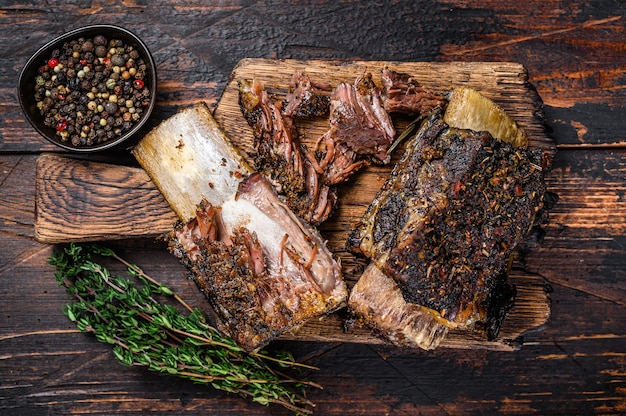 Costillas de ternera a la barbacoa con hierbas y cuchillo de carnicero. Fondo de madera oscura. Vista superior.