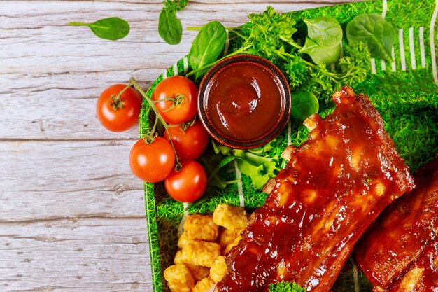 Costillas de ternera con salsa barbacoa y vegetales sobre tabla de madera.