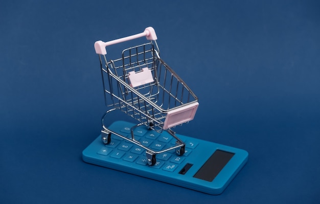 Costo de mercado. Mini carrito de la compra con calculadora sobre fondo azul clásico