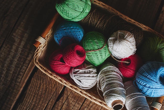 Costura, macramé, tejido de punto. Hilos e hilos de colores vivos en una cesta de mimbre sobre un fondo de madera. Pasatiempo de las mujeres.