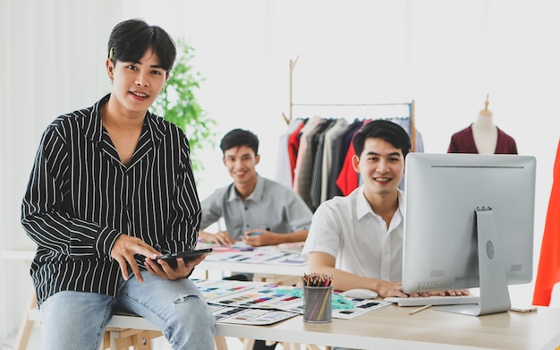 Costureira asiática usando um tablet perto de colegas do sexo masculino, navegando dados no computador e desenhando um esboço