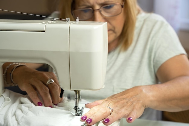 Costureira de mulher com óculos concentrando-se enquanto costura na máquina de costura