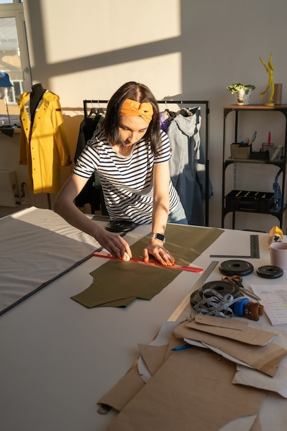 Foto costureira desenha padrões de papel em têxteis com giz e régua. designer de roupas trabalha em estúdio