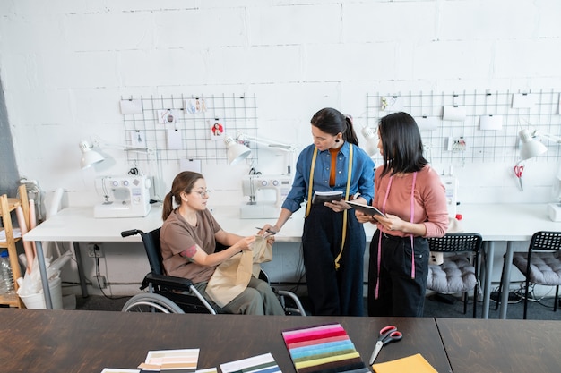 Costureira e designers discutindo têxteis para novos modelos de moda em oficina