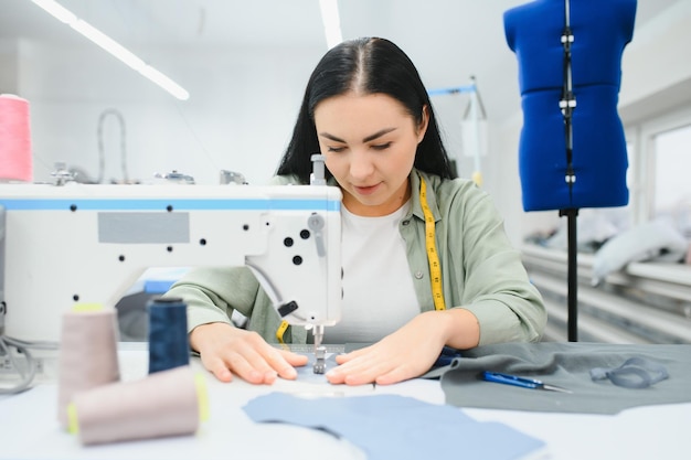 Costureira feminina feliz trabalhando com máquina de costura na fábrica têxtil