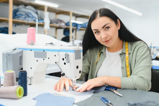 Costureira feminina feliz trabalhando com máquina de costura na fábrica têxtil