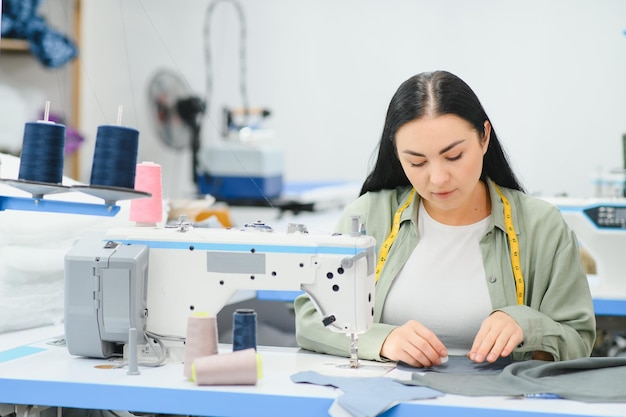 Costureira feminina feliz trabalhando com máquina de costura na fábrica têxtil