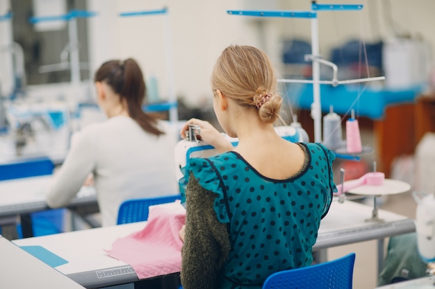 Costureira linda jovem costura na máquina de costura na fábrica