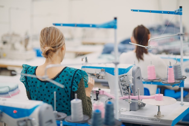 Costureira linda jovem costura na máquina de costura na fábrica