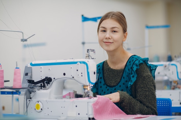 Costureira linda jovem costura na máquina de costura na fábrica