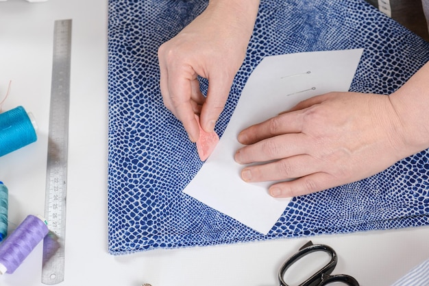 Costureira marca uma peça de roupa em um tecido com giz de acordo com um padrão de papel