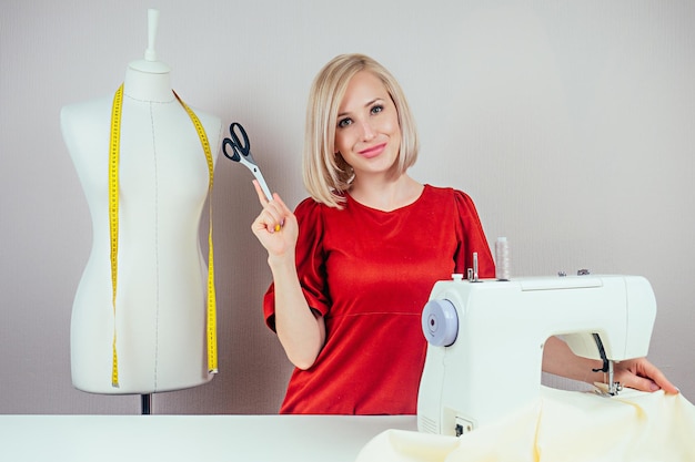 Costureira sorridente trabalhando com tesoura e máquina de costura no fundo do manequim com a fita métrica amarela e fundo branco