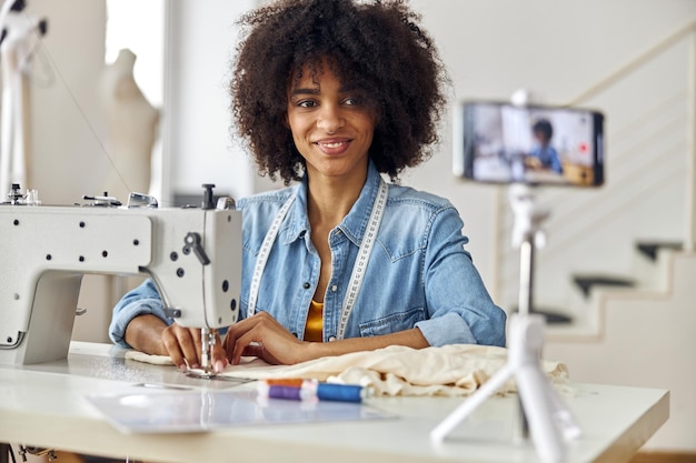 Costurera afroamericana cose ropa con una moderna máquina de disparar una lección de video en el taller