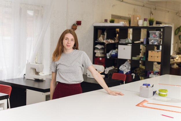 Una costurera feliz en un estudio de costura posando. Retrato de una bella costurera llevando una cinta métrica y trabajando en una fábrica textil