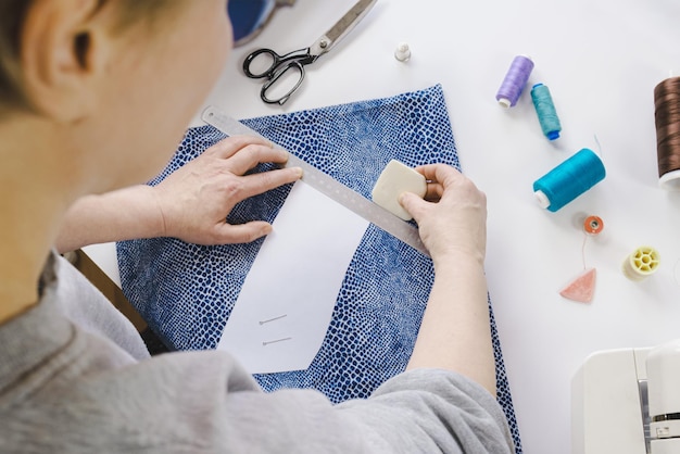 Costurera marca una prenda de vestir en una tela con una tiza de acuerdo con un patrón de papel El trabajo de un sastre herramientas para coser y crear ropa Enfoque selectivo de primer plano borroso