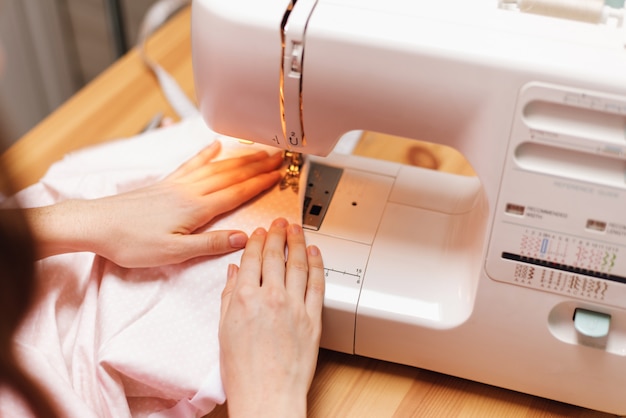 Costurera trabaja en una máquina de coser. La mujer cose y sostiene una tela rosa.