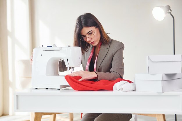 Costurera trabaja con tela roja Mujer joven en ropa formal está en el interior Concepción de estilo