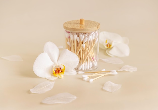 Cotonetes de bambu em uma jarra perto de flores de orquídeas brancas em produto de cuidados com a pele ecologicamente correto bege claro