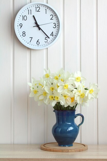 Cottage-Interieur mit einem Strauß weißer Narzissen und einer runden Wanduhr. Gartenfrühlingsblumen