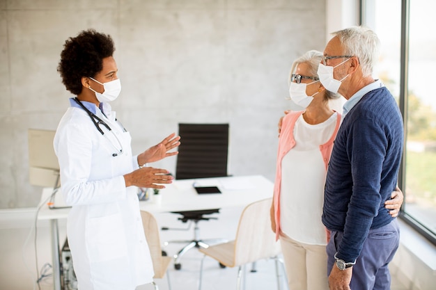 Coule sênior com máscaras faciais protetoras recebe notícias de médica negra no consultório