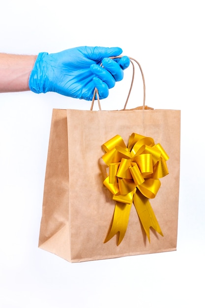 Courier com luvas azuis segura uma sacola de presente com laço dourado