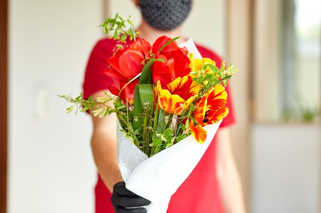Courier, entregador de luvas médicas de látex entrega com segurança as compras on-line de um buquê de flores