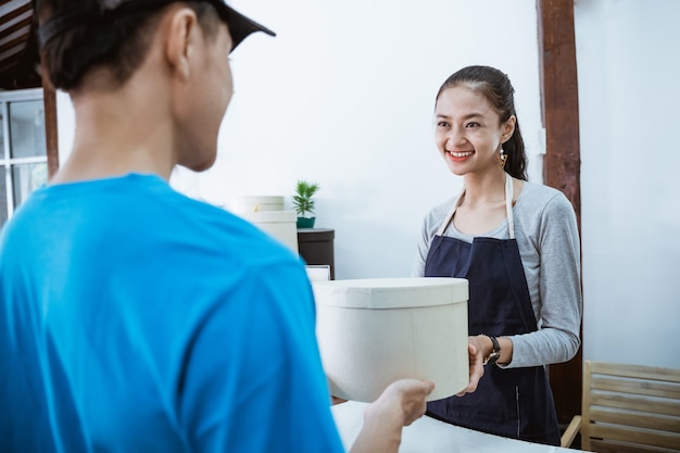 Foto courier retrato sonriendo traer el paquete para la joven comerciante que recibe un paquete de courier