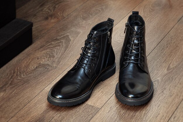 Couro de botas pretas para homens no interior em um piso de madeira isolado no fundo branco