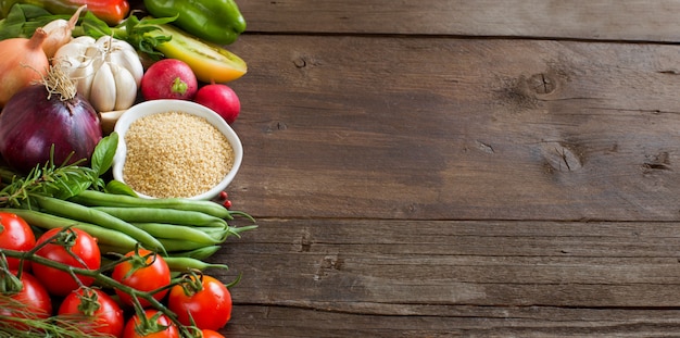 CousCous in einer Schüssel und frisches Gemüse auf einem braunen Holztisch schließen oben