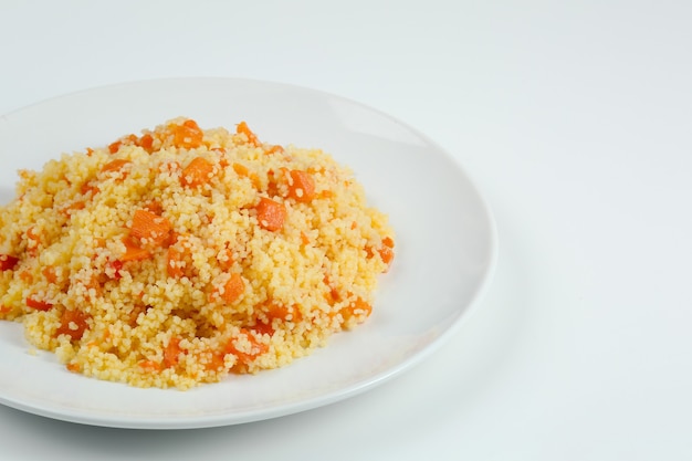 Couscous mit Karotten in weißer Plattennahaufnahme. Couccous isoliert auf weißem Hintergrund