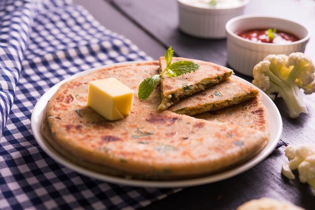 Couve-flor recheada ou Gobi Paratha é um pão achatado indiano. menu de café da manhã ou almoço favorito no norte da Índia, servido sobre um fundo sombrio com requeijão e ketchup de tomate em uma tigela