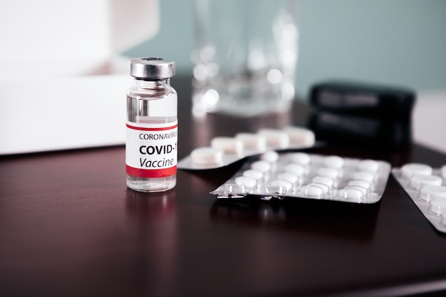 COVID-19 Ampullen mit Impfstoff und Pillen auf einem Tisch. Gesundheitswesen und medizinisches Konzept.
