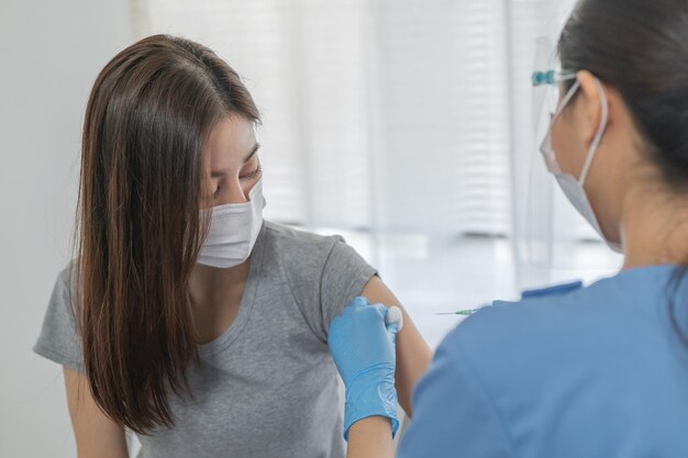 Covid-19, Coronavirus-Hand einer jungen Krankenschwester, Arzt, der einen Spritzenimpfstoff gibt, injiziert dem Patienten des asiatischen Arms einen Schuss. Impfung, Immunisierung oder Krankheitsprävention gegen Grippe- oder Viruspandemiekonzept.