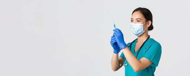 Covid-19, Coronavirus-Krankheit, Konzept für Gesundheitspersonal. Seitenansicht einer selbstbewusst lächelnden asiatischen Ärztin, Krankenschwester bereiten Spritze mit Impfstoff gegen Grippeimpfung vor, stehender weißer Hintergrund.