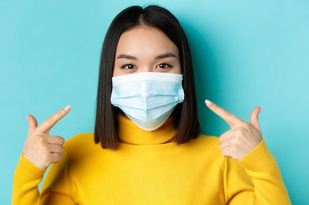 Covid-19, distanciamento social e conceito de pandemia. Perto de uma jovem mulher asiática usando máscara médica durante o coronavírus, em pé sobre um fundo azul.