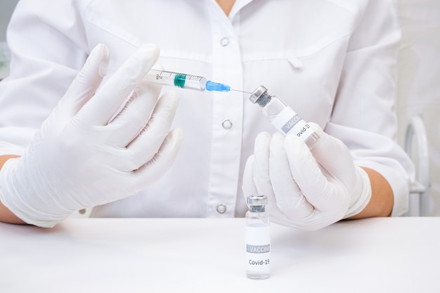 COVID-19-Impfstoff in Forscherhänden, Ärztin hält Spritze und Flasche mit Impfstoff zur Heilung von Coronaviren. Konzept der Behandlung des Koronavirus, der Injektion, des Schusses und der klinischen Studie während der Pandemie.