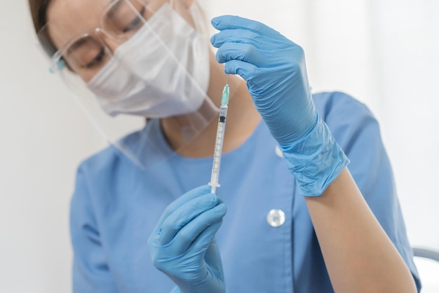 Covid-19, la mano coronavirus de una joven médica o enfermera asiática prepara la inyección de la vacuna con jeringa para el paciente, el dolor. Vacunación, inmunización o prevención de enfermedades contra la gripe o el concepto de pandemia de virus.