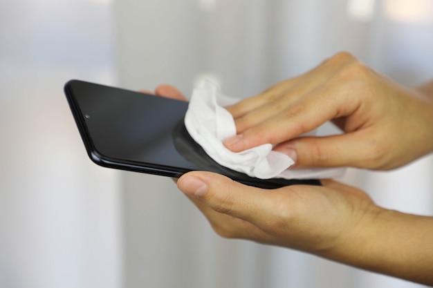 COVID-19 Mulher com Coronavírus pandêmico, limpando com lenços umedecidos Desinfecção da tela do smartphone contra doença por coronavírus em 2019