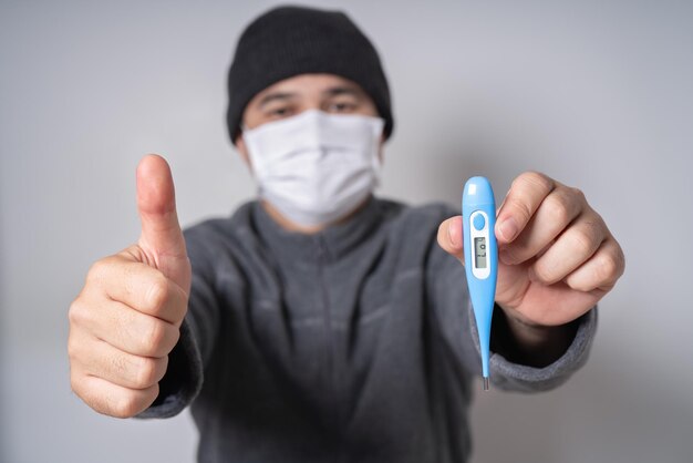 COVID 19 Pandemia Coronavirus protegendo o vírus da doença, verificando com o termômetro clínico Homem usando máscara branca facial