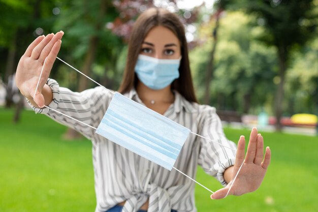 COVID-19, pandemia, equipo de protección, tratamiento de manos: una mujer de cabello oscuro con equipo de protección personal y camisa blanca sostiene una máscara en los brazos abiertos.