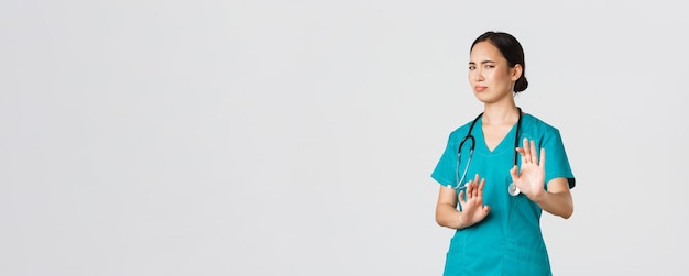 Covid-19, profissionais de saúde, conceito de pandemia. Enfermeira asiática engraçada relutante, médico evitando alguém, se afaste e mostre o gesto de parada, fazendo careta ou encolhendo-se ao rejeitar uma oferta horrível, recusar