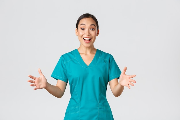 Covid-19, trabajadores de la salud, concepto de pandemia. Enfermera asiática feliz y sorprendida en matorrales levantando las manos emocionadas y sonrientes. El doctor felicita con buenas noticias, aplausos, fondo blanco.