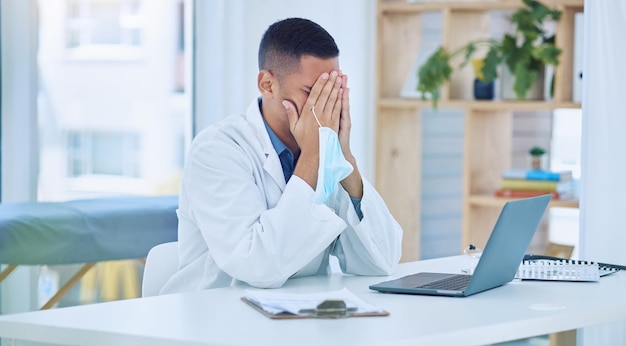 Covid-Arzt müde im Büro von Stress und Gesichtsmaske in der Hand, nachdem er einen Bericht auf dem Laptop mit Patienteninformationsdokumenten geschrieben hatte Coronavirus-Mediziner Burnout und erschöpft von covid19